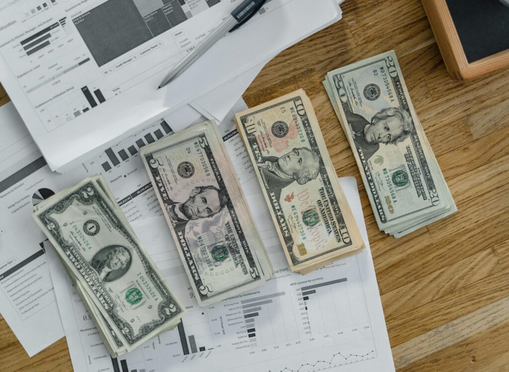 Stacks of US Dollar banknotes placed over financial documents and reports on a desk.